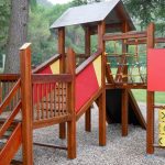 Colorful wooden playground set in an outdoor park setting under tall trees.