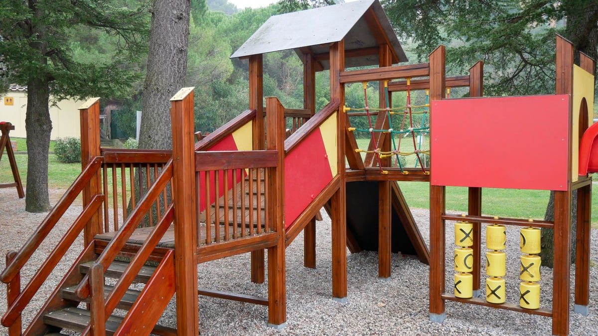 Colorful wooden playground set in an outdoor park setting under tall trees.