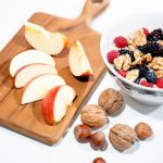 A vibrant breakfast bowl with mixed berries, walnuts, and apple slices on a rustic board.